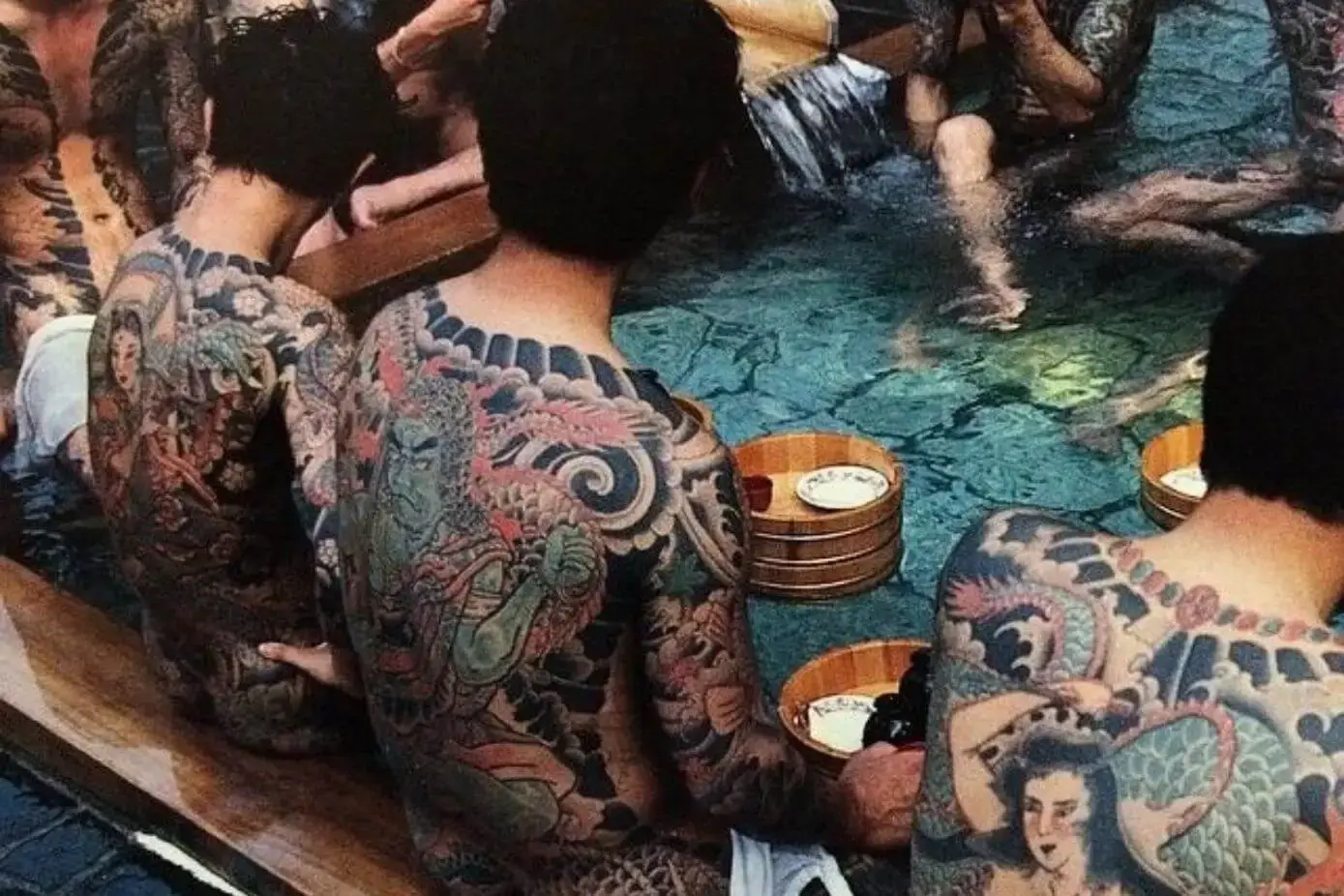 A group of people covered with tattoos soaking in a japanese onsen bath